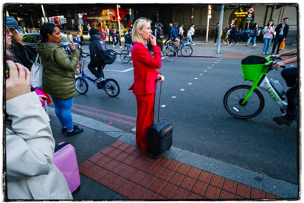 A lady dressed in red waits pensively to cross the road outside of london bridge station